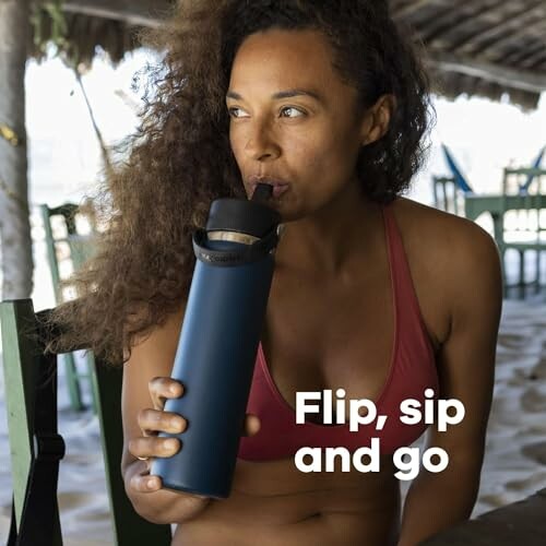 Woman in swimsuit drinking from a bottle at the beach.