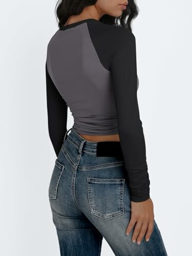Woman wearing a black and gray long-sleeve top with jeans, viewed from the back.