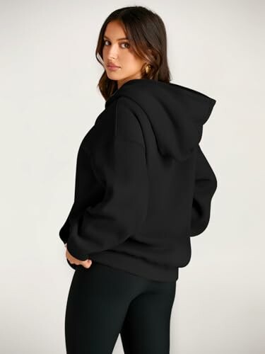 Woman wearing a black hoodie, looking over her shoulder.