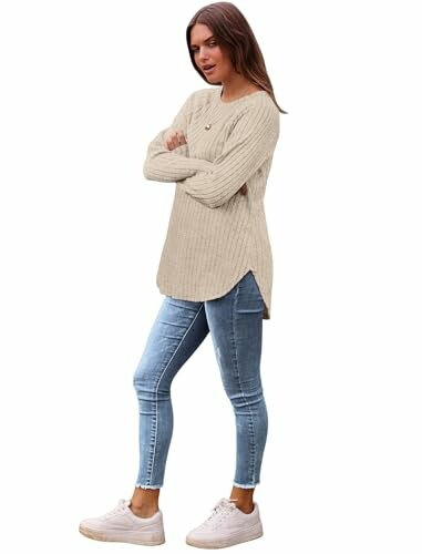 Woman in beige sweater and jeans standing with arms crossed