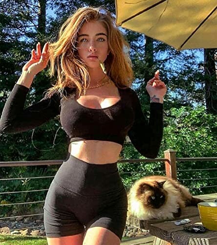 Woman in black outfit standing outdoors with a cat on a table.